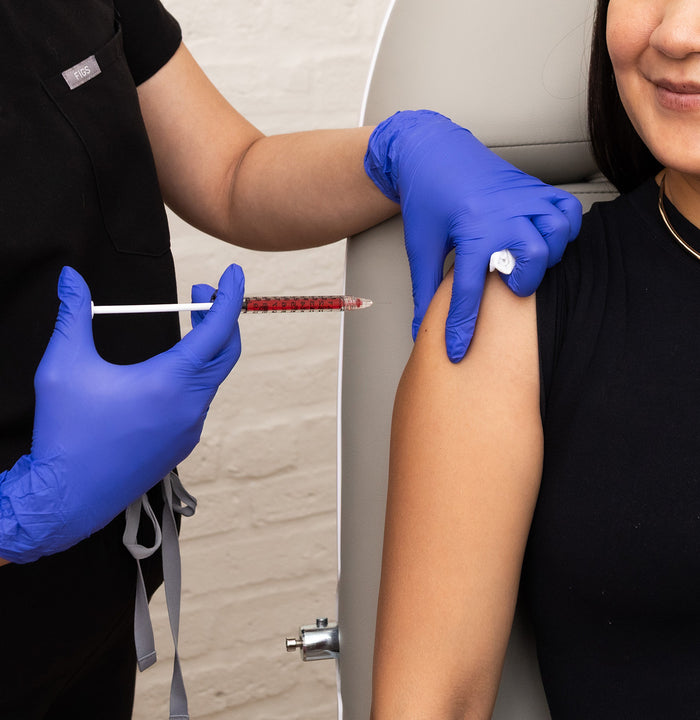 Person receiving a shot from a healthcare professional wearing blue gloves.