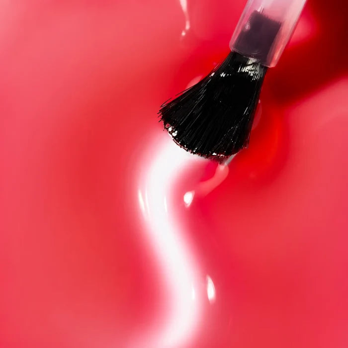 A nail polish brush hovering over a pool of translucent candy pink Bio Peptide Nail Glow.