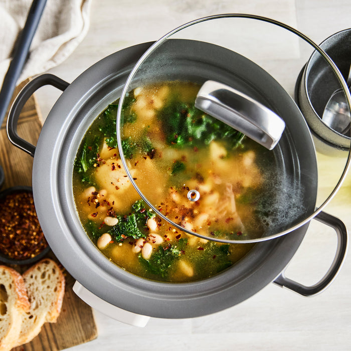 Macadamia-colored 4-quart slow cooker with browning feature cooking vegetable soup, next to sliced bread.