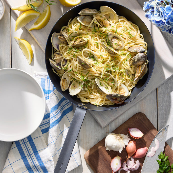 Clam pasta in a Bobby Flay by GreenPan carbon steel pan, served on a white table.