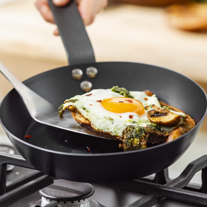 Fried egg with mushrooms and greens on toast being lifted from a GreenPan 10-inch carbon steel frypan.