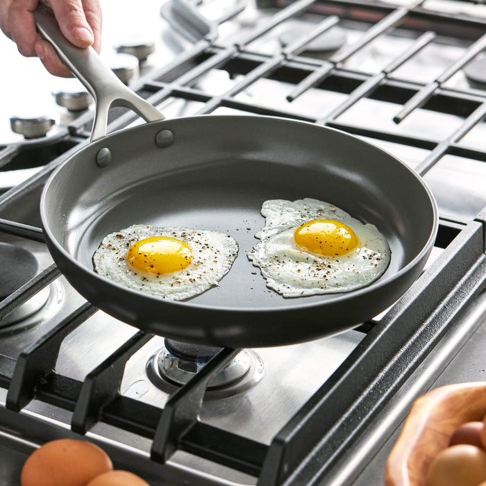 Two eggs cooking in a black hard-anodized frypan on a gas stove.