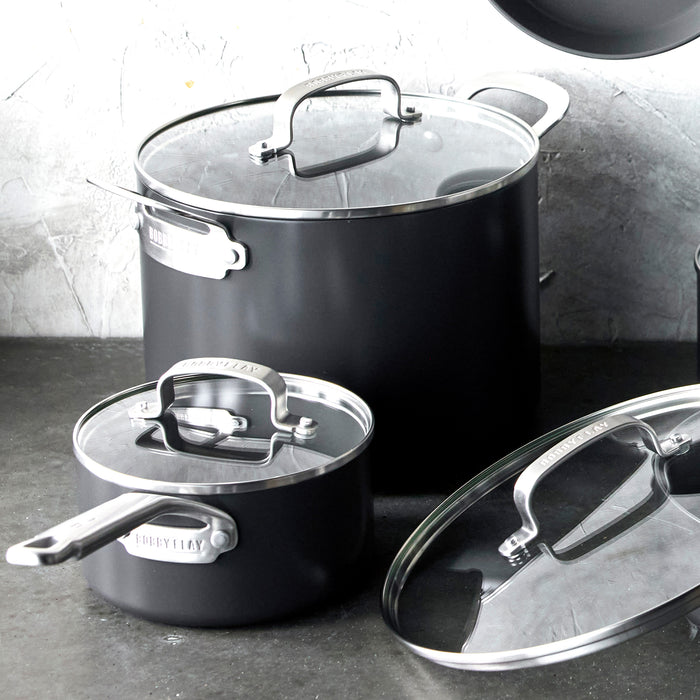 Two stainless steel pots with glass lids on a dark countertop; one lid is resting beside its pot.