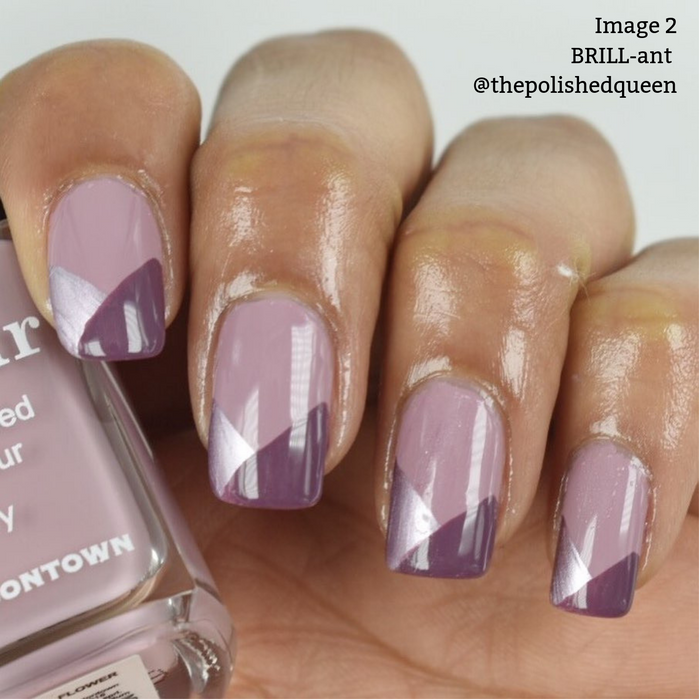 A hand with manicured nails in a geometric design, featuring shades of purple and lavender, accented with metallic-rose nail polish. The person is holding a bottle of 16+ Free, vegan cruelty-free nail polish from LONDONTOWN labeled "BRILL-ant." Text on the upper right reads "Image 2 BRILL-ant @thepolishedqueen.