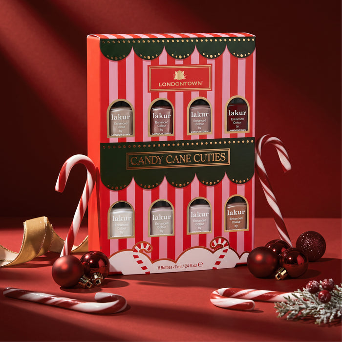 A box of LONDONTOWN’s Candy Cane Cuties Holiday Set is displayed alongside candy canes, red ornaments, and festive decorations on a vibrant red background—making it the perfect holiday gift or curated gift set for the season.