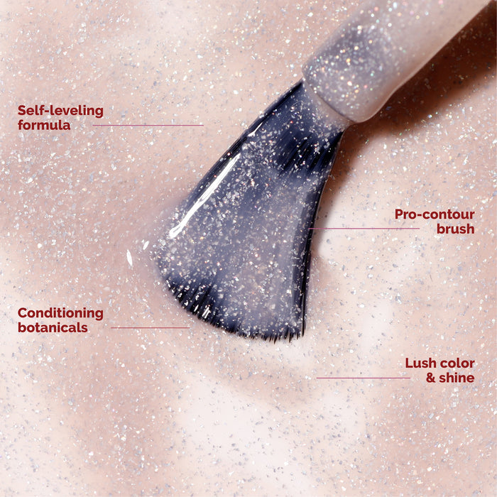 Close-up of a nail polish brush with glittery light pink polish from the LONDONTOWN Candy Cane Cuties Holiday Set; labeled features include a self-leveling formula, conditioning botanicals, pro-contour brush, and lush color and shine—making it an ideal choice for a curated gift set or thoughtful holiday present.