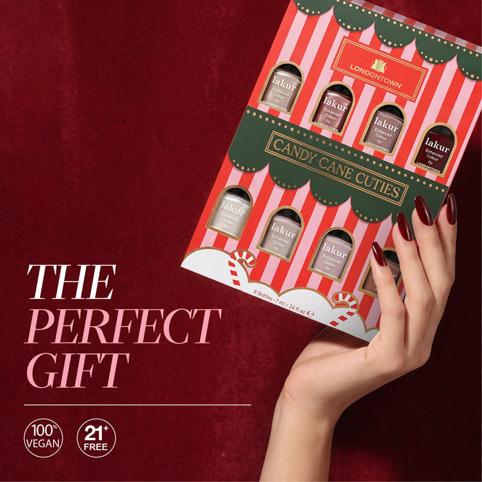 A hand with dark red nails holds the LONDONTOWN Candy Cane Cuties Holiday Set against a red background, with the text “The Perfect Gift.”.