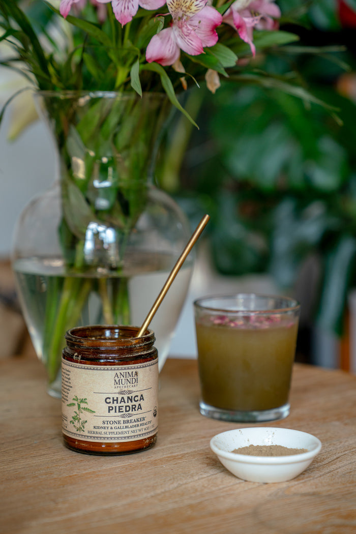 Jar of 'Chana Piedra' on a wooden table with a glass of juice and flowers in the background