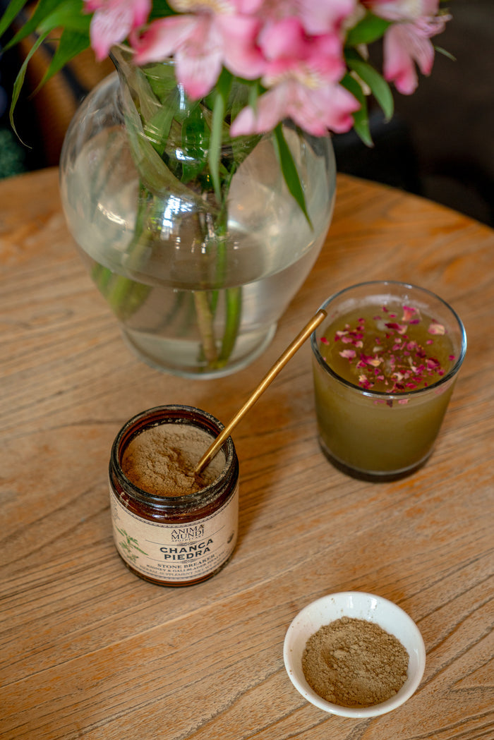 Jar of chaga spice, small bowl with spice, glass with green liquid and flowers on a wooden table