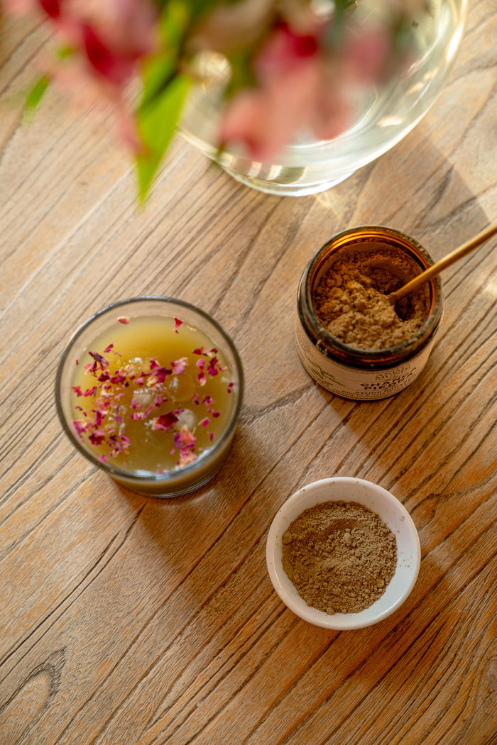 Spice jar, small bowl, and glass with floral elements on a wooden surface.