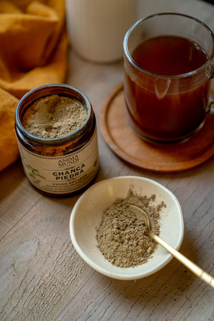 Jar of Chaga Piedra powder, bowl with powder, and glass of tea on a wooden surface