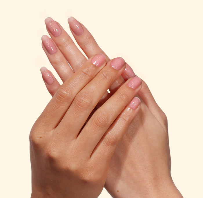 Two hands with well-groomed nails painted in LONDONTOWN’s Confetti Cake—a pastel pink shade—are held together against a plain light background, giving the scene a sweet and delicate touch.