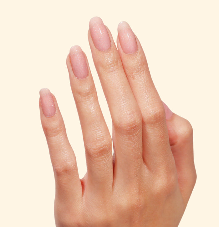 A hand with neatly manicured, natural-looking nails is shown against a plain, light background, the tips dusted with the soft pastel pink confetti sparkle of LONDONTOWN’s Confetti Cake.