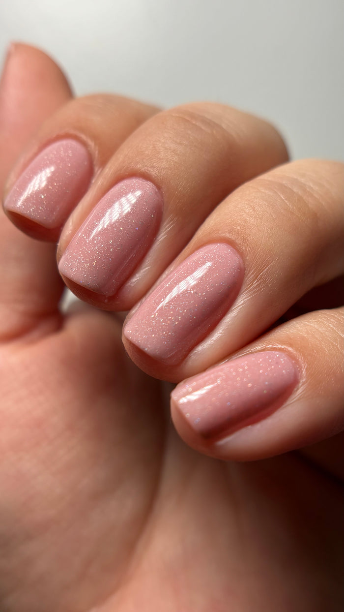 A close-up of a hand with neatly manicured nails painted in LONDONTOWN’s Confetti Cake, a sweet pastel pink polish featuring a subtle confetti sparkle.