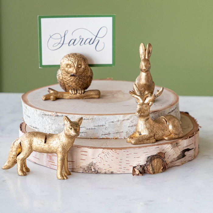 An Owl, Rabbit, Fox and Deer place card holder stacked on cylinders of wood with the Dark Green Frame Place Card with "Sarah" written on it in cursive, being held up by a slot in the owl's back.