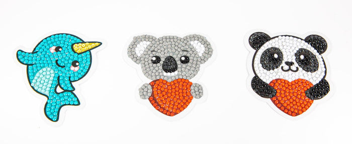 The Diamond Dotz Love You Chums Stickers kit features three beaded stickers: a smiling blue narwhal, gray koala, and black-and-white panda, each holding a red-orange heart on a white background.