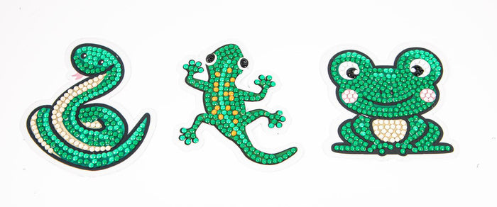 The Diamond Dotz Slip n Slide by Diamond Dotz features three cartoon-style stickers—a coiled green snake, a green gecko with orange spots, and a smiling green frog—all decorated with sparkling gemstones.