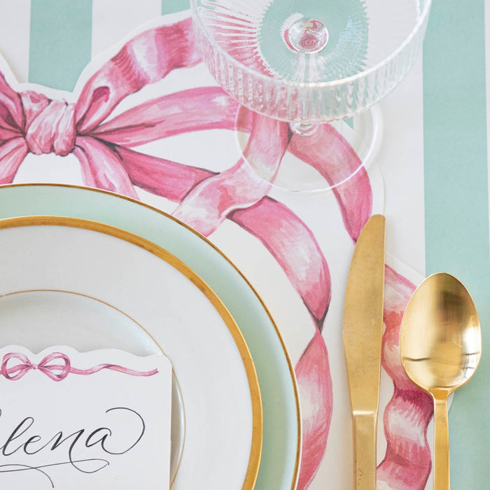 A whimsy place setting with a gold spoon and fork on a Hester & Cook Die-cut Pink Bow Placemat.