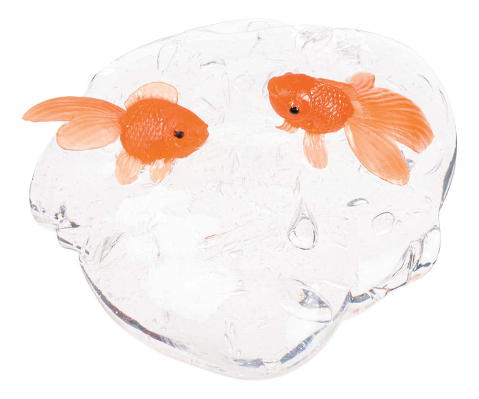 The Farm Fresh Fish Bowl Slime by Farm Fresh features two orange goldfish figurines swimming atop clear, glass-like slime shaped like a water puddle with water droplet details, creating a playful sensory toy.