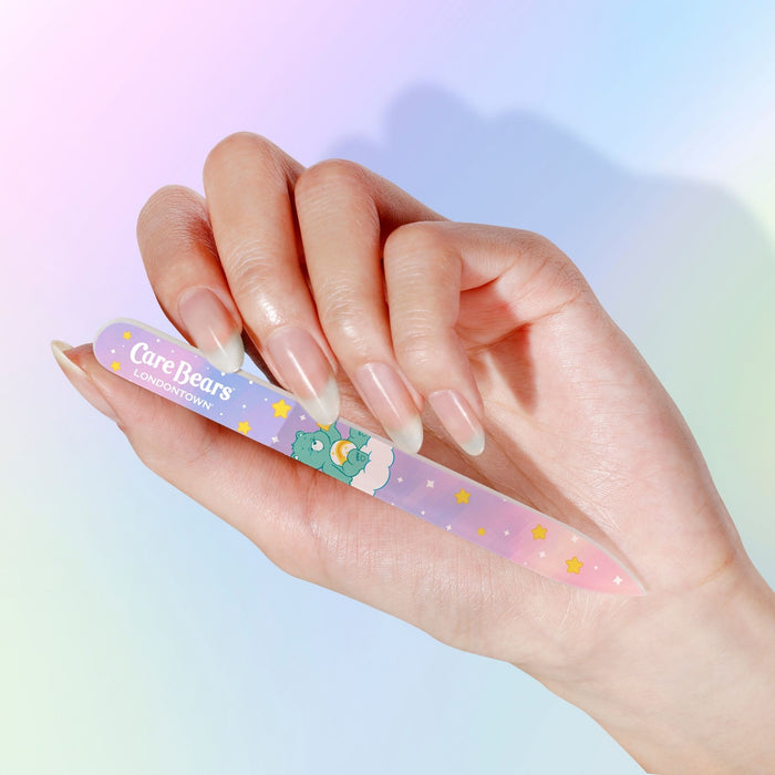 A hand holds the LONDONTOWN Glass Nail File - Wish Bear, featuring pastel colors, stars, and a bear design against a soft gradient background—ideal for gentle, damage-free nail care.