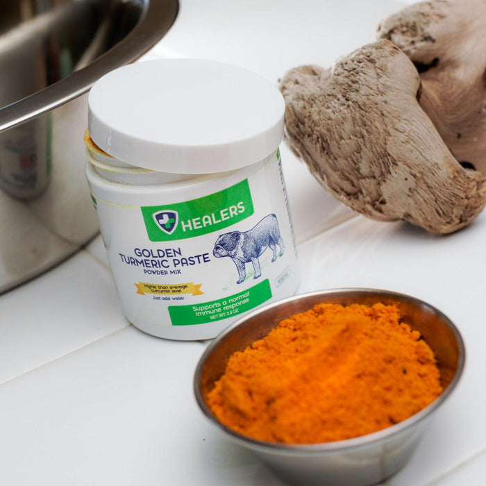 White jar of Healers Golden Turmeric Paste, bowl of turmeric, and ginger root. Kitchen counter with stainless steel sink. Product is for pets.