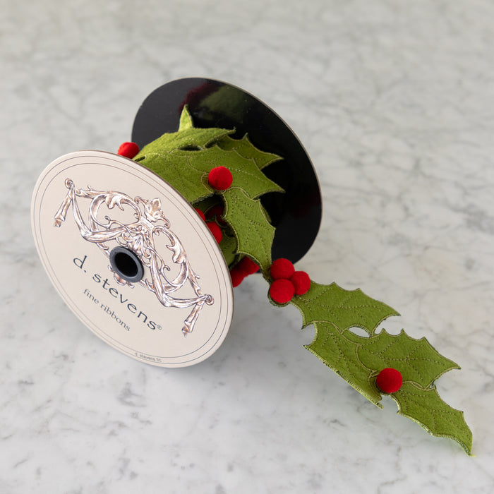 Spool of green ribbon with red berries and 'd. stevens' label on a marble surface.