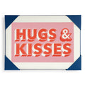 A greeting card with 'HUGS & KISSES' written in bold, red letters on a pink background, bordered with blue, and meant for various occasions.