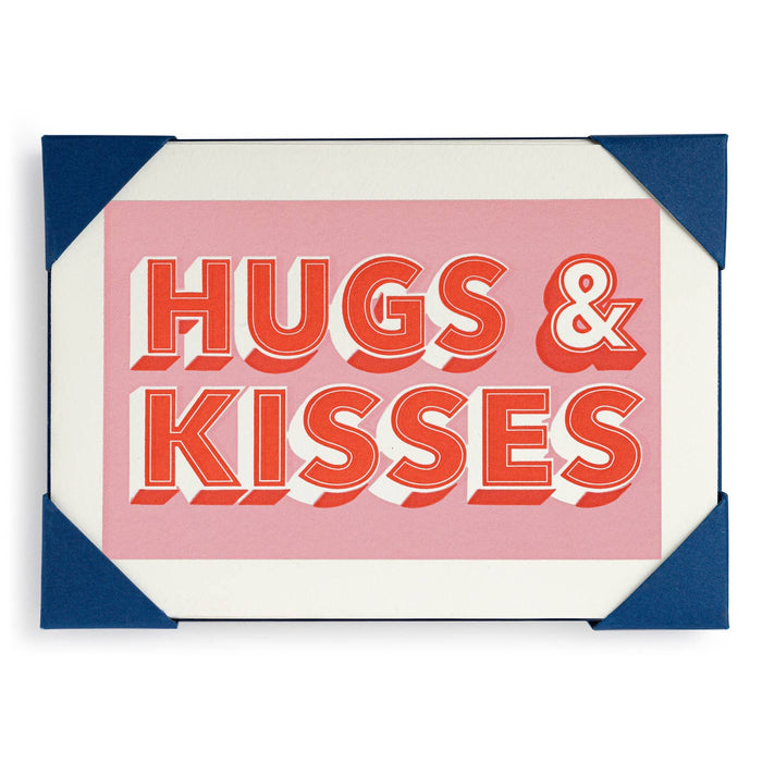 A greeting card with 'HUGS & KISSES' written in bold, red letters on a pink background, bordered with blue, and meant for various occasions.
