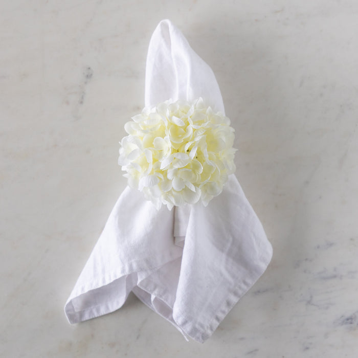 White napkin with a cream Hydrangea Napkin Ring around it, on a marble surface.