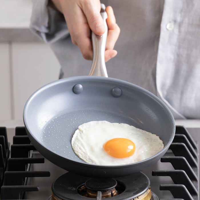 A fried egg cooks in a green ceramic nonstick frypan on a stove, with a bamboo spatula beside the egg.