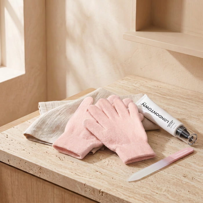 The LONDONTOWN Mani Perfect Spa Gloves, paired with a beige cloth, a tube of hand cream, and a glass nail file arranged on a light stone surface in natural light, invite soothing moments of hand care into your daily downtime.