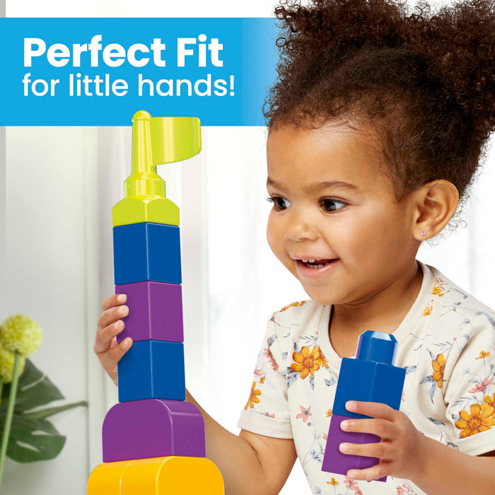 A young child with curly hair smiles while playing with the MEGA Bloks Even Bigger Building Bag by Mega Bloks, enhancing fine motor skills. Text reads Perfect Fit for little hands! in the upper left corner. A plant is visible in the background.
