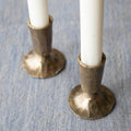 Two bronze Creative Co-Op metal taper holders holding candles on a table.