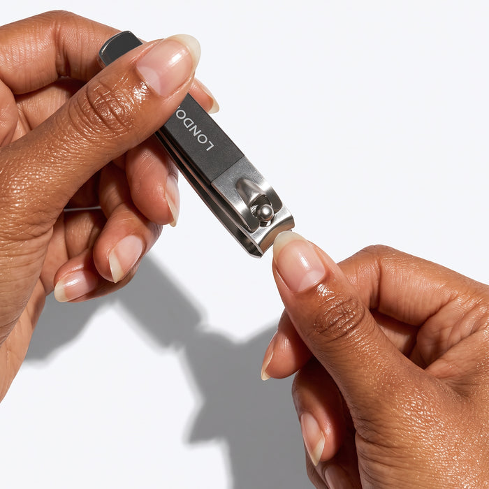 A person uses the LONDONTOWN Nail Clipper Duo Set - Black to achieve a clean cut while trimming the fingernails on their left hand against a white background.