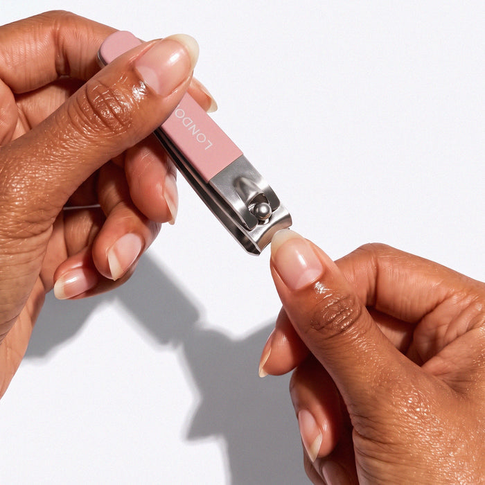 A person trims their fingernail with the LONDONTOWN Nail Clipper Duo Set - Pink, featuring two sizes and pink handles, for a precise, clean cut against a white background.