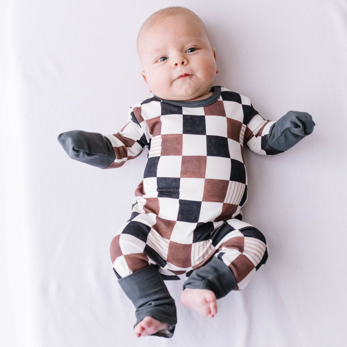 A baby lying down wearing a checkered patterned romper with long sleeves and footies.