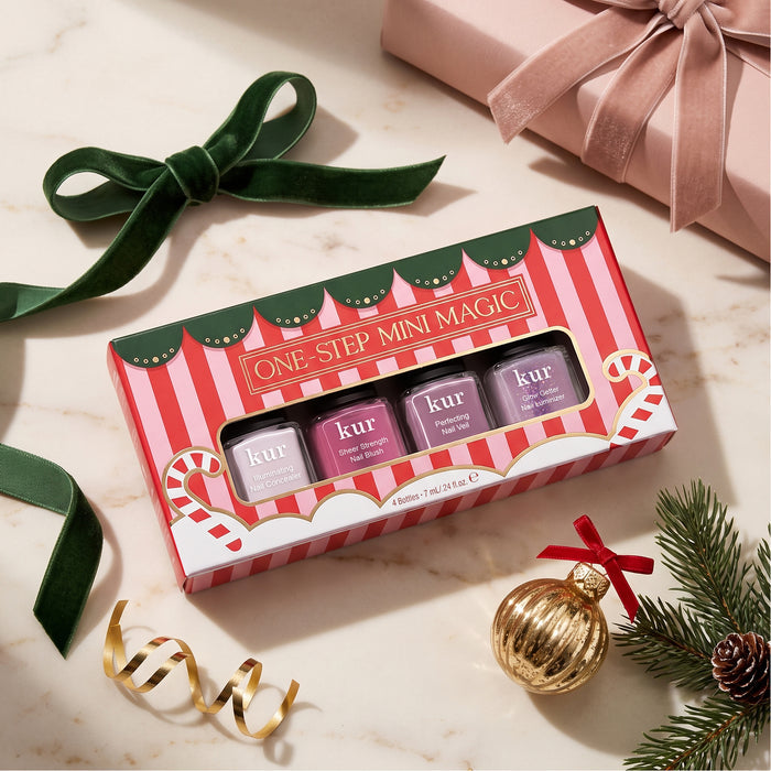 A festive boxed set of four LONDONTOWN One Step Mini Magic nail polishes sits on a marble surface with a green ribbon, gold ornament, and wrapped gift nearby, making it the perfect holiday set for effortless one-step manicures.