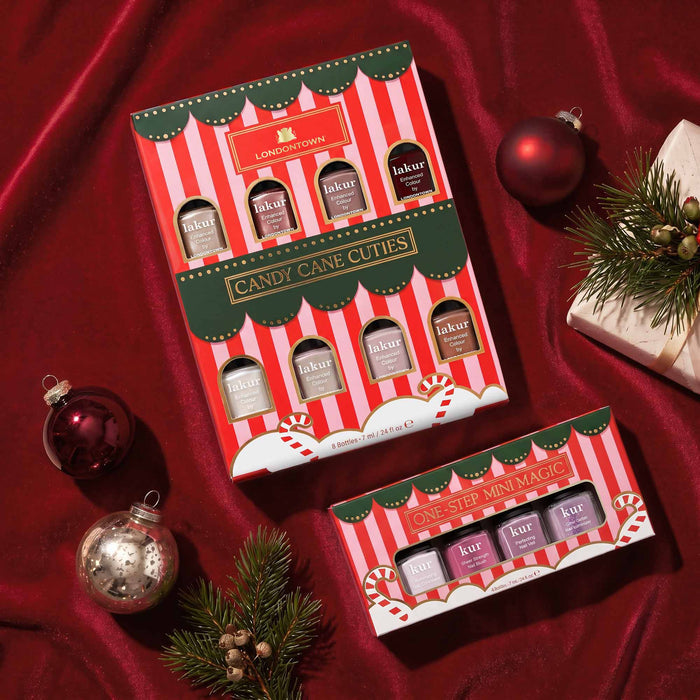 LONDONTOWN’s One Step Mini Magic nail polish gift sets, featuring vibrant red and white packaging, are artfully displayed with Christmas ornaments, pine branches, and a wrapped present on a brown surface—making them the perfect holiday set for effortless one-step manicures.