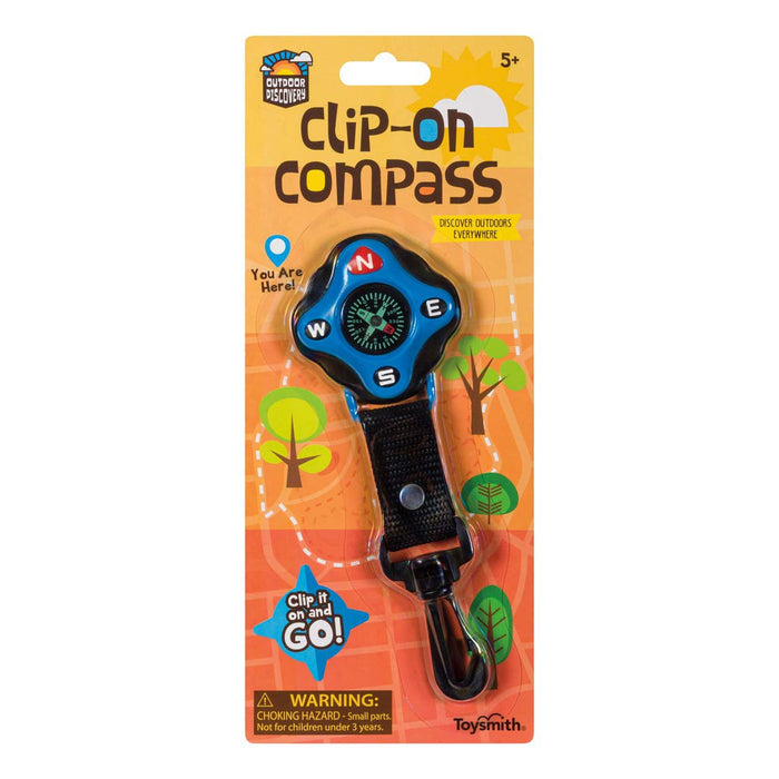 The Outdoor Discovery Clip On Compass by Outdoor Discovery is a kids' compass with a black strap and plastic clip, packaged on an orange card featuring outdoor-themed graphics, safety warnings, and labeled "Clip-On Compass.