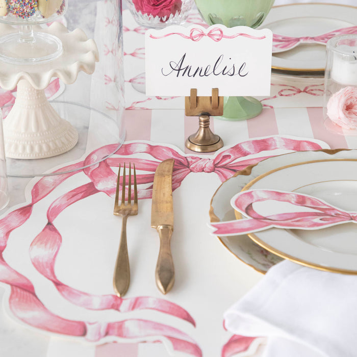 A table with dishes and silverware adorned with Hester & Cook's Pink Bow Place Card.