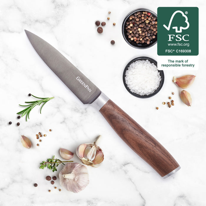 Titanium paring knife with walnut handle next to garlic, herbs, salt, and pepper on a countertop.