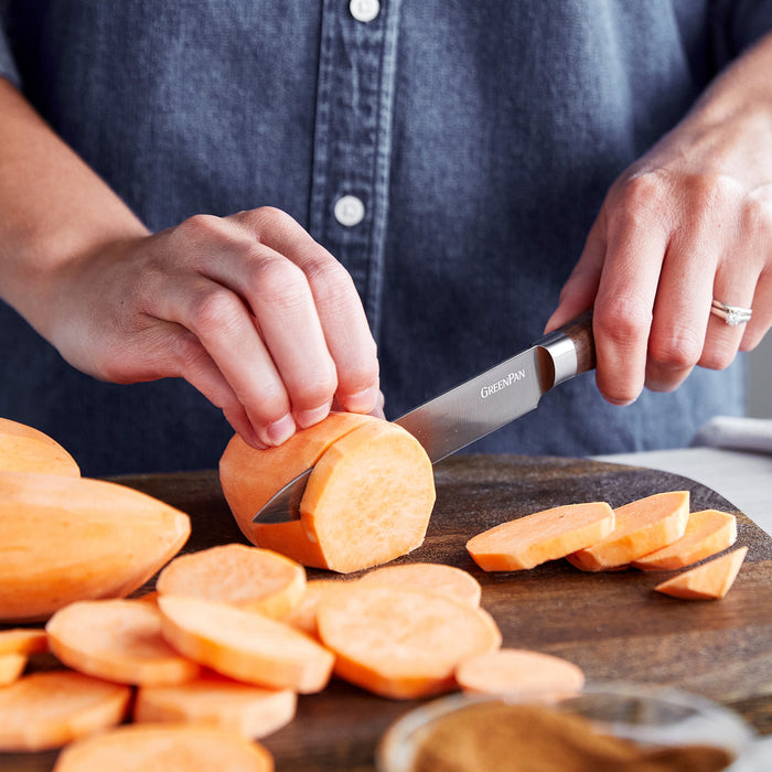 Slicing a sweet potato with a 5 utility knife featuring a walnut handle on a wooden cutting board.