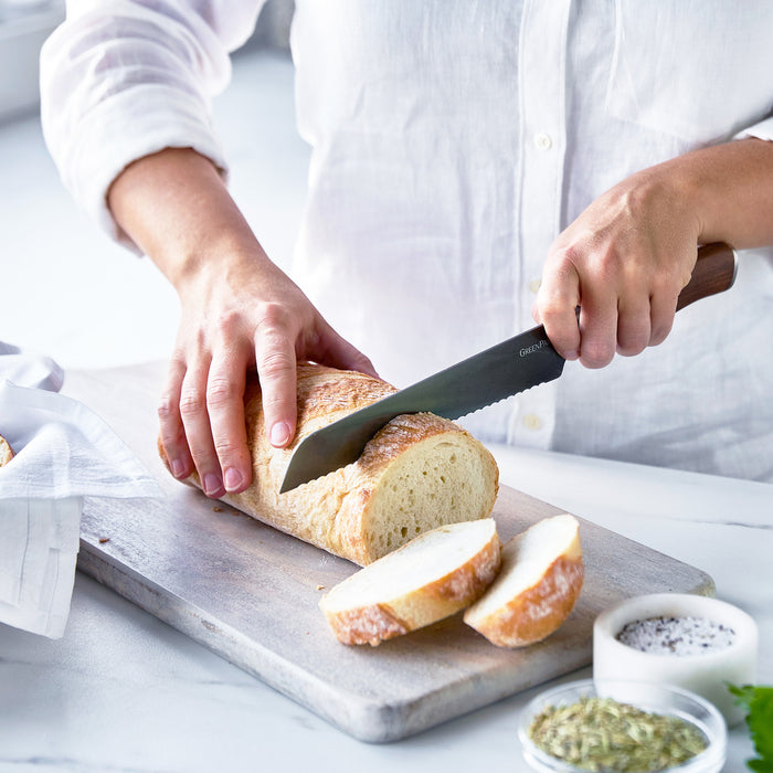 Slicing bread with an 8 bread knife featuring a walnut handle on a cutting board, with spices nearby.