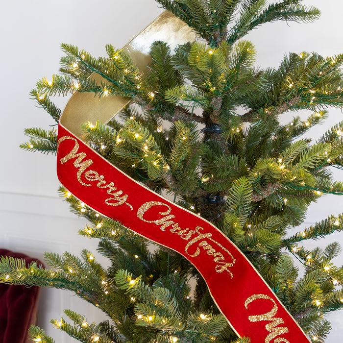 Decorative red ribbon with 'Merry Christmas' on a lit Christmas tree.