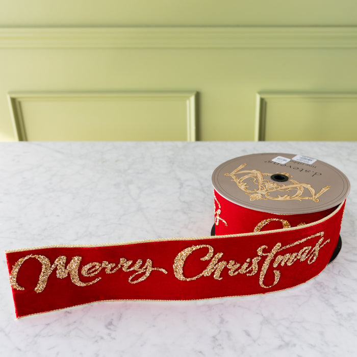 Red ribbon with 'Merry Christmas' text and a spool on a white surface.
