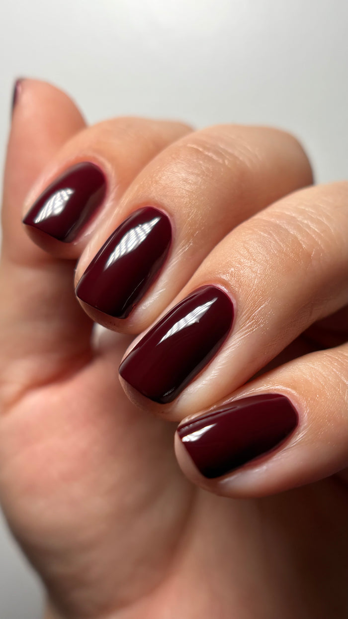 A hand with neatly manicured nails painted in LONDONTOWN’s Red Velvet, a deep burgundy, glossy color.