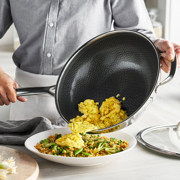 Scrambled eggs being added from a black ceramic nonstick wok into a pan of vegetable fried rice.