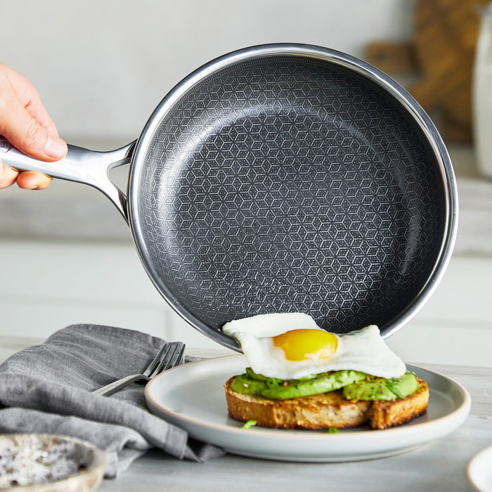 Hand tipping an 8-inch gray ceramic nonstick frypan to slide a fried egg onto avocado toast.