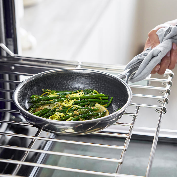 Hand lifting a black ceramic nonstick frypan with sautéed vegetables from the oven using a cloth.