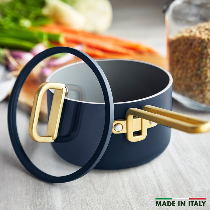 Blue ceramic nonstick saucepan with gold handle and lid, next to assorted vegetables.